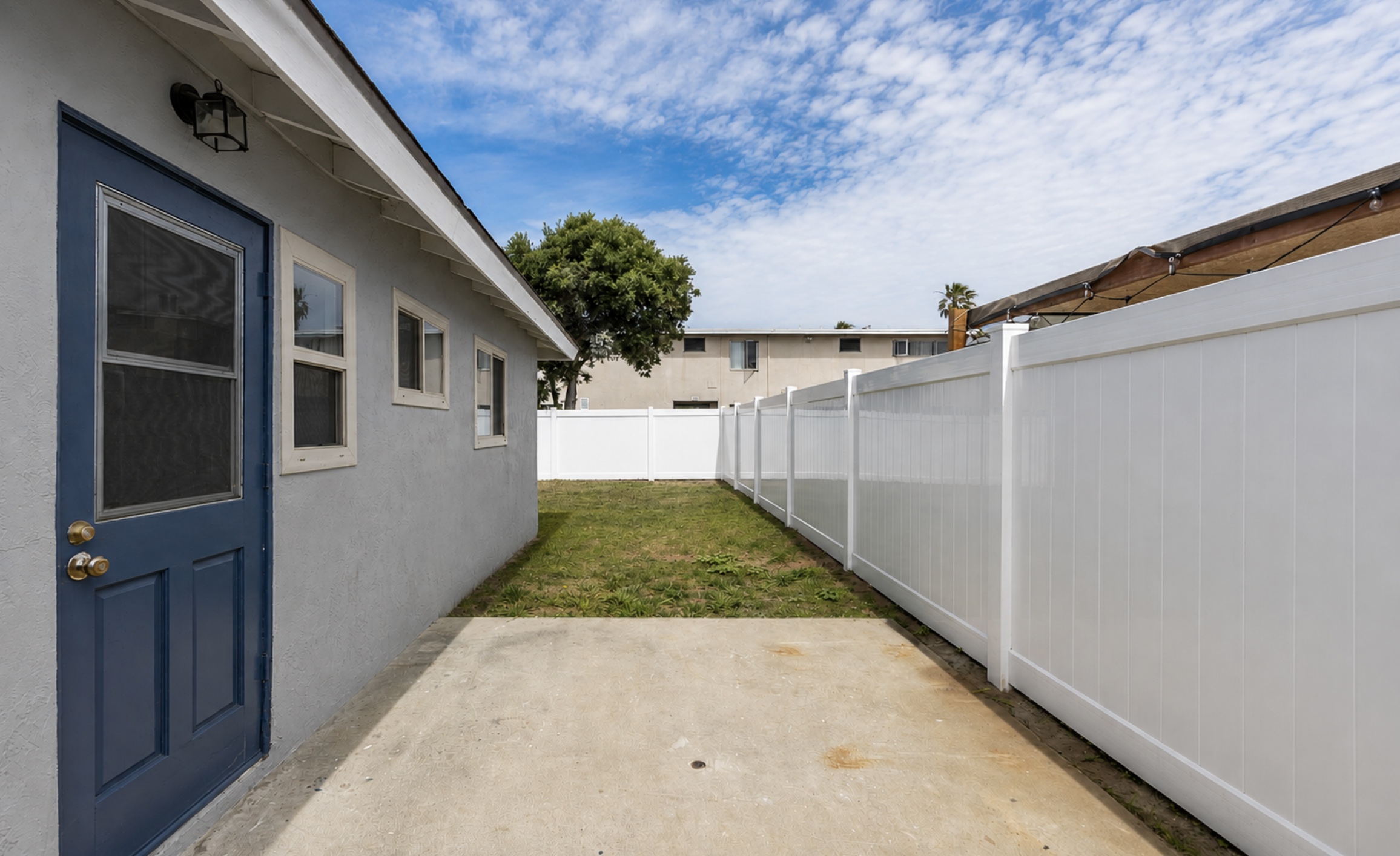 Gallery Private fenced backyard with concrete walkway, side entrance, and lawn at The Dahlia Coastal Bungalows.
