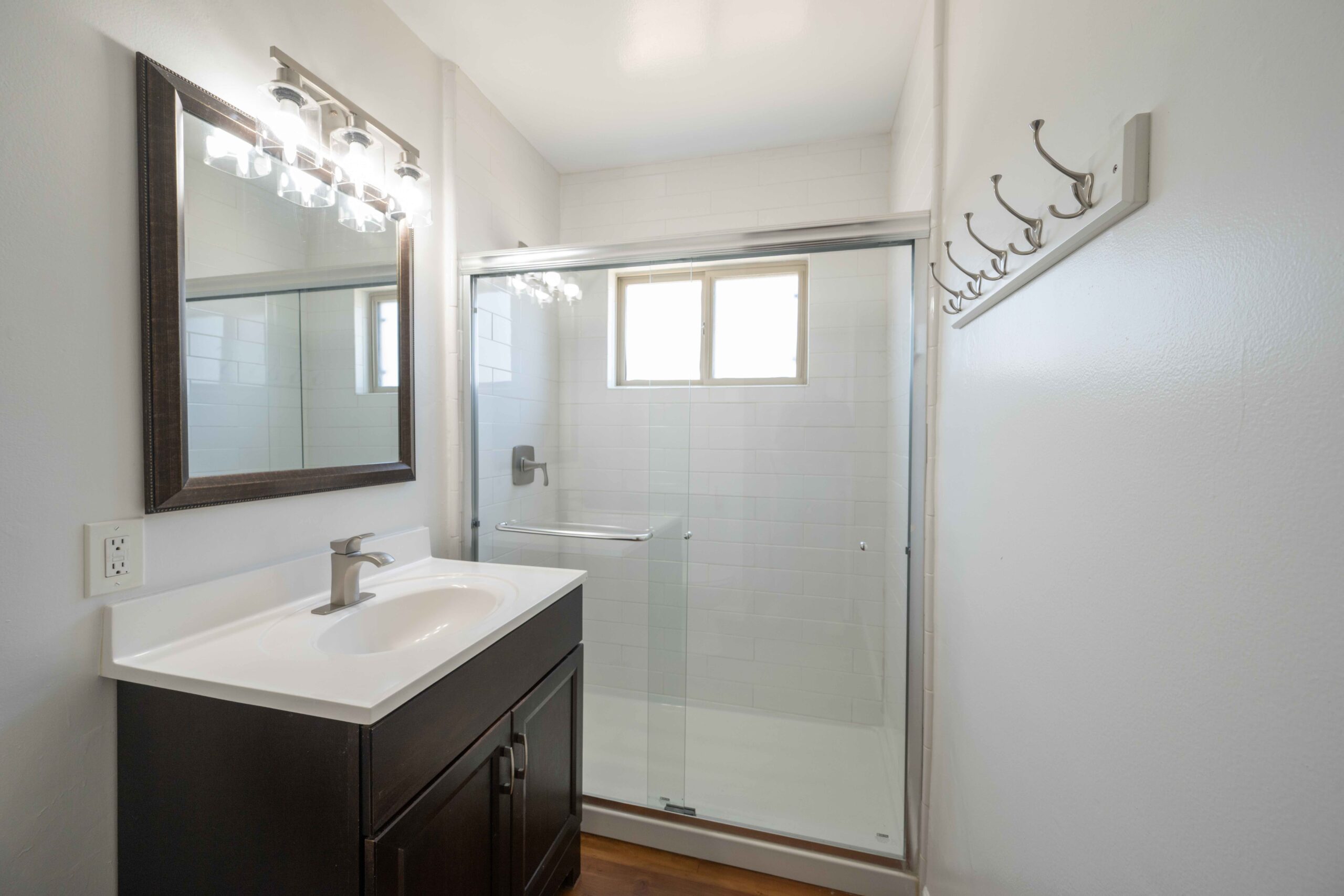 Gallery Renovated bathroom with a modern vanity, tiled walk-in shower, glass shower doors, and wall-mounted coat hooks.