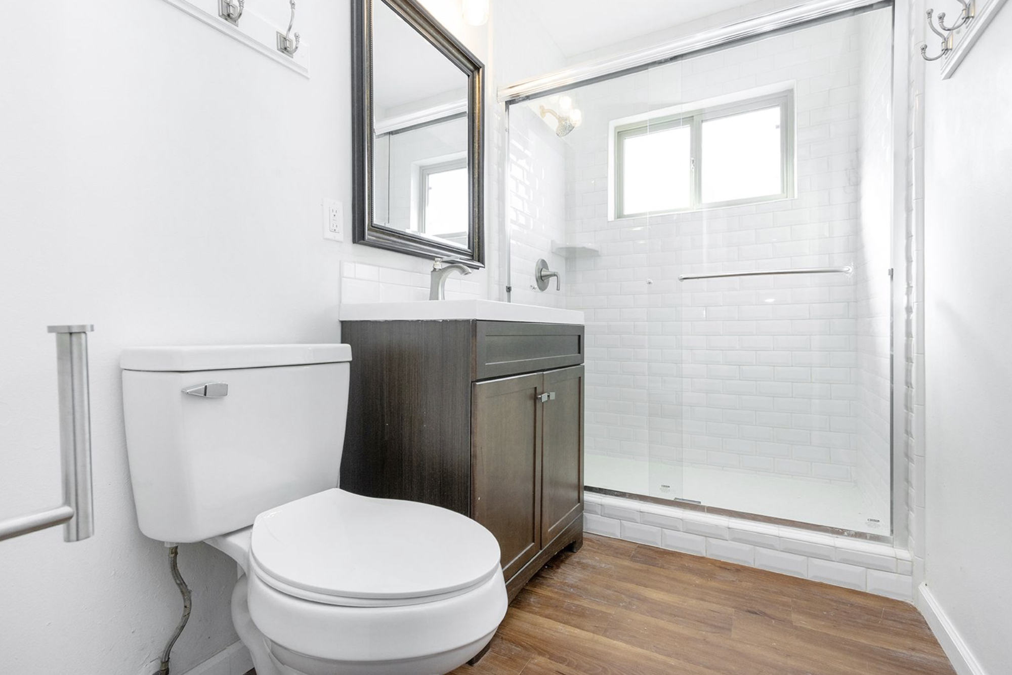 Gallery Renovated bathroom featuring a dark wood vanity, toilet, and tiled walk-in shower with glass doors.