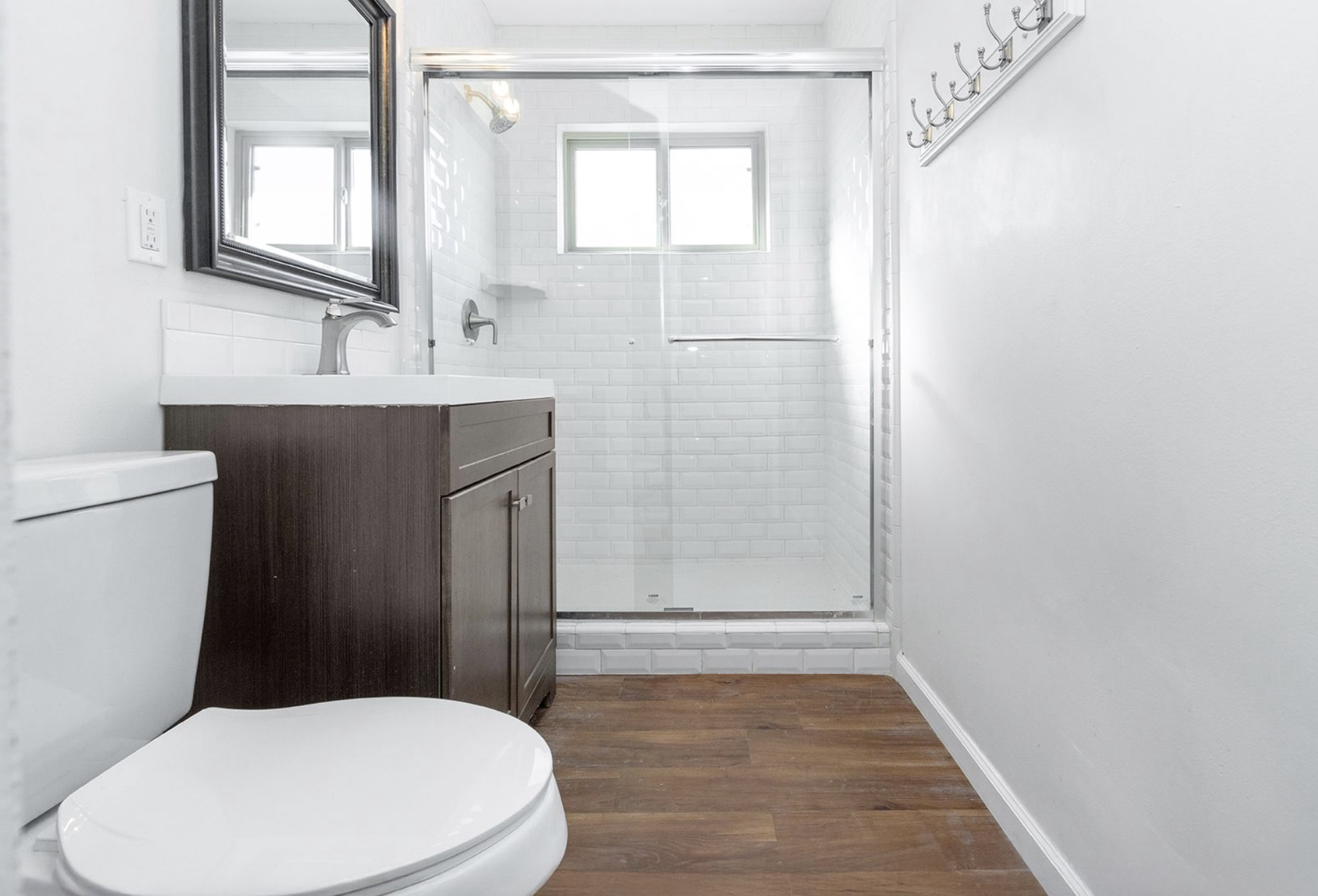 Gallery Bathroom with dark wood vanity, tiled walk-in shower, glass doors, and a bright modern interior.
