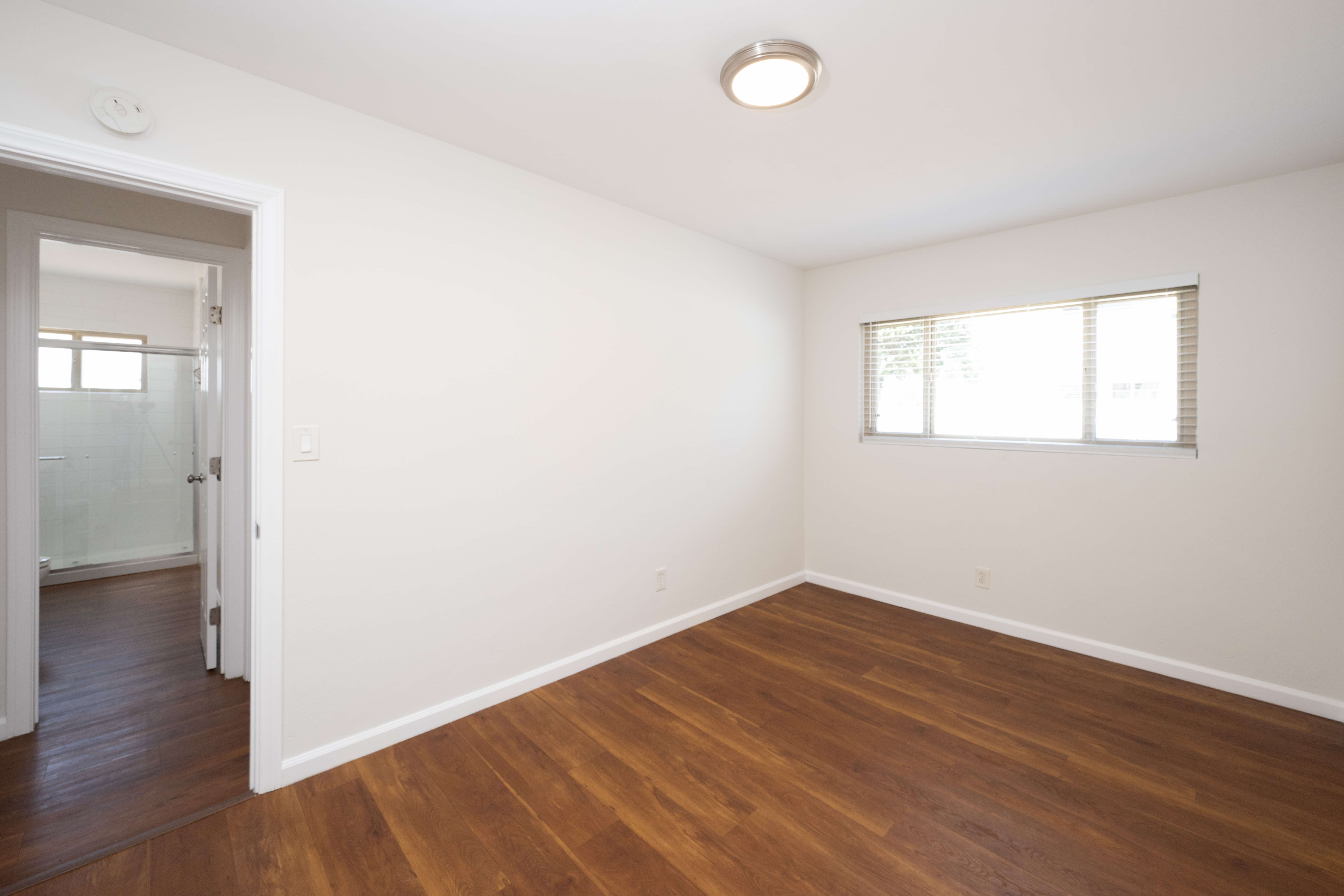 Gallery Renovated bedroom with wood-look flooring, window, and doorway to bathroom.