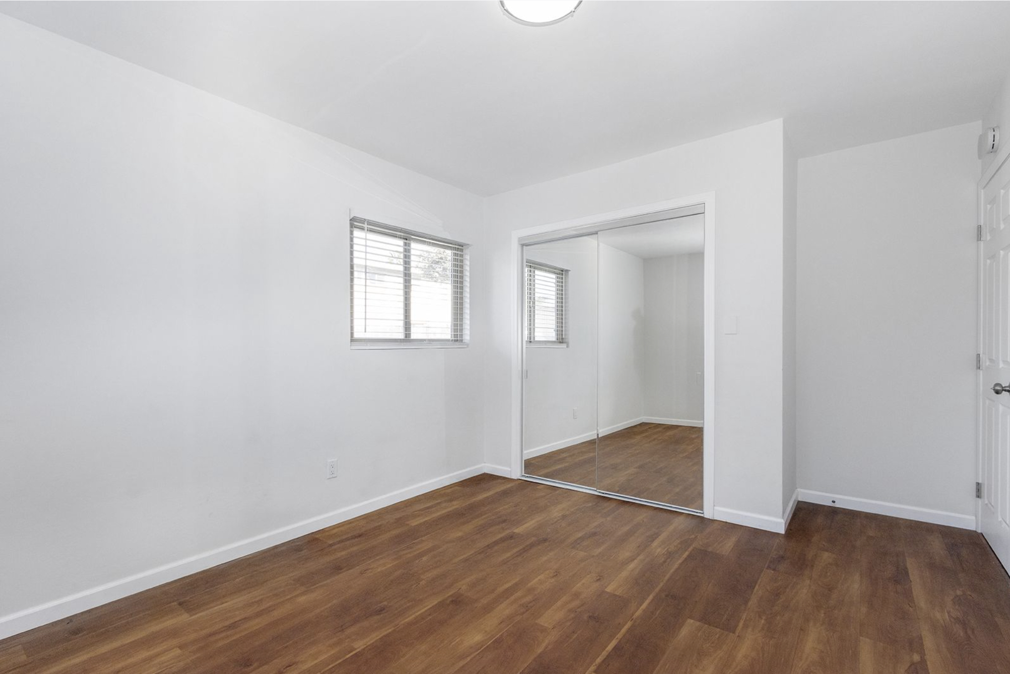 Gallery Renovated bedroom with wood-look flooring, mirrored wardrobe doors, and natural light.
