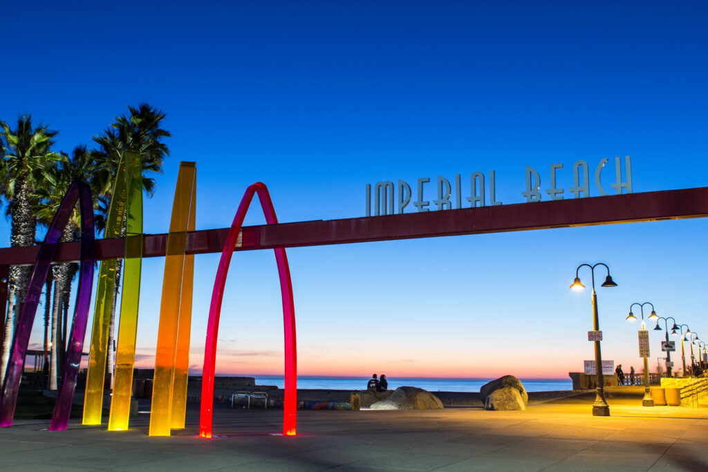 Home Imperial Beach entrance sign overlooking the Pacific Ocean with colorful coastal sculptures and palm trees.