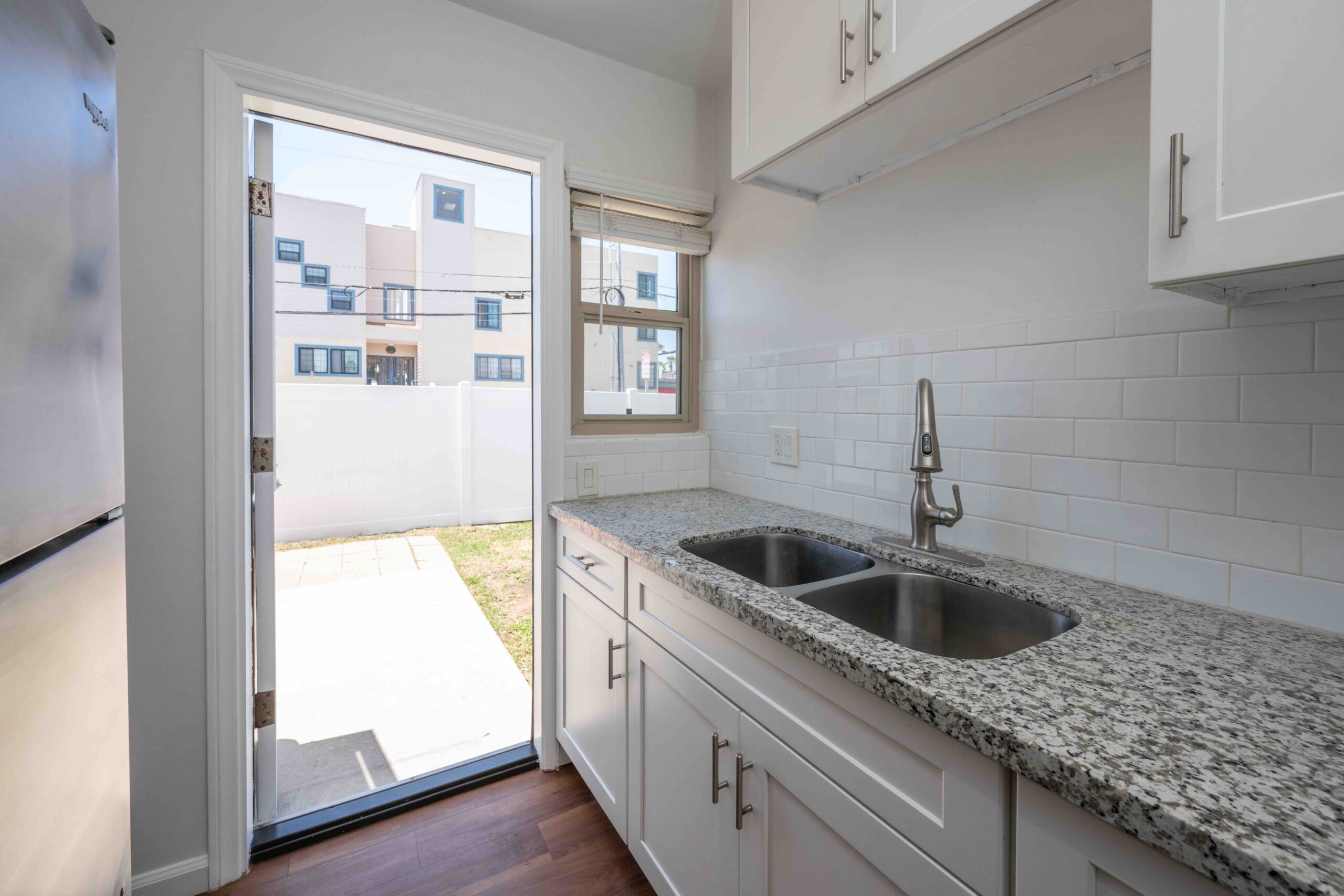Gallery Renovated kitchen with granite countertops, double sink, and door leading to fenced backyard.